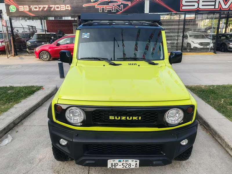 Suzuki Jimny verde lima de frente bajo el techo de papel picado del lote